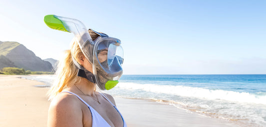 Girl on the beach wearing a full face snorkel mask.